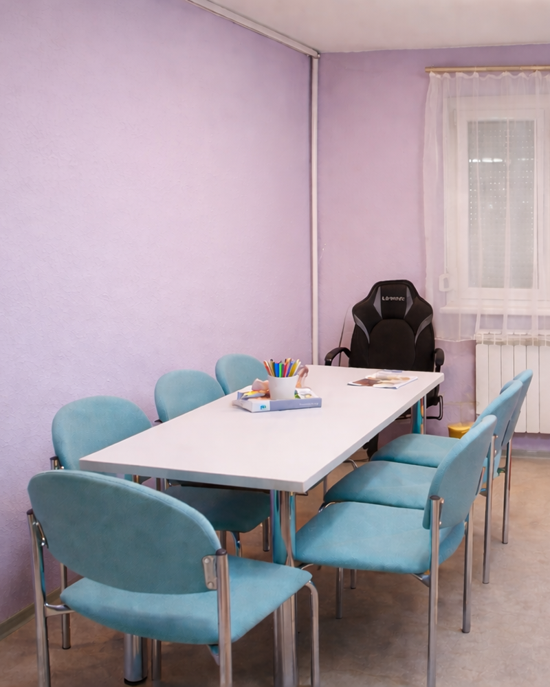 Tanulószoba fehér asztallal és türkiz székekkel, ahol Zsuzsi a diákokat fogadja.